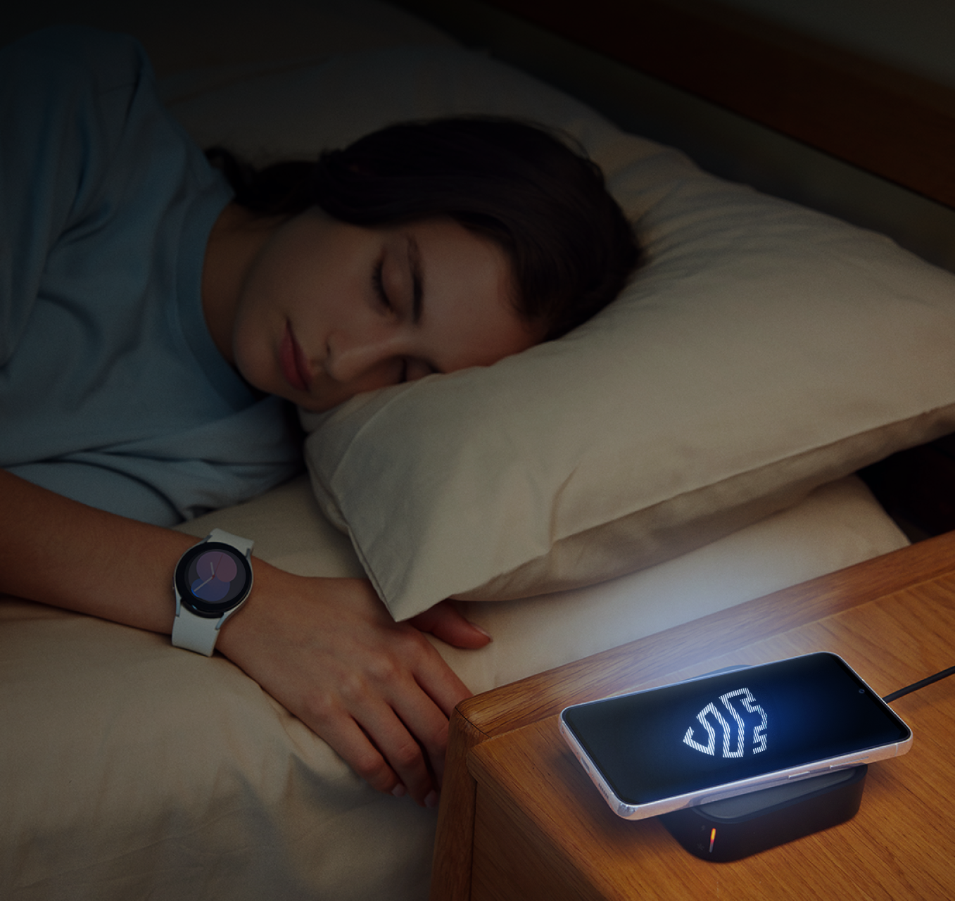 Persona durmiendo en la oscuridad junto a un dispositivo móvil Samsung que muestra un logotipo de Knox iluminado.