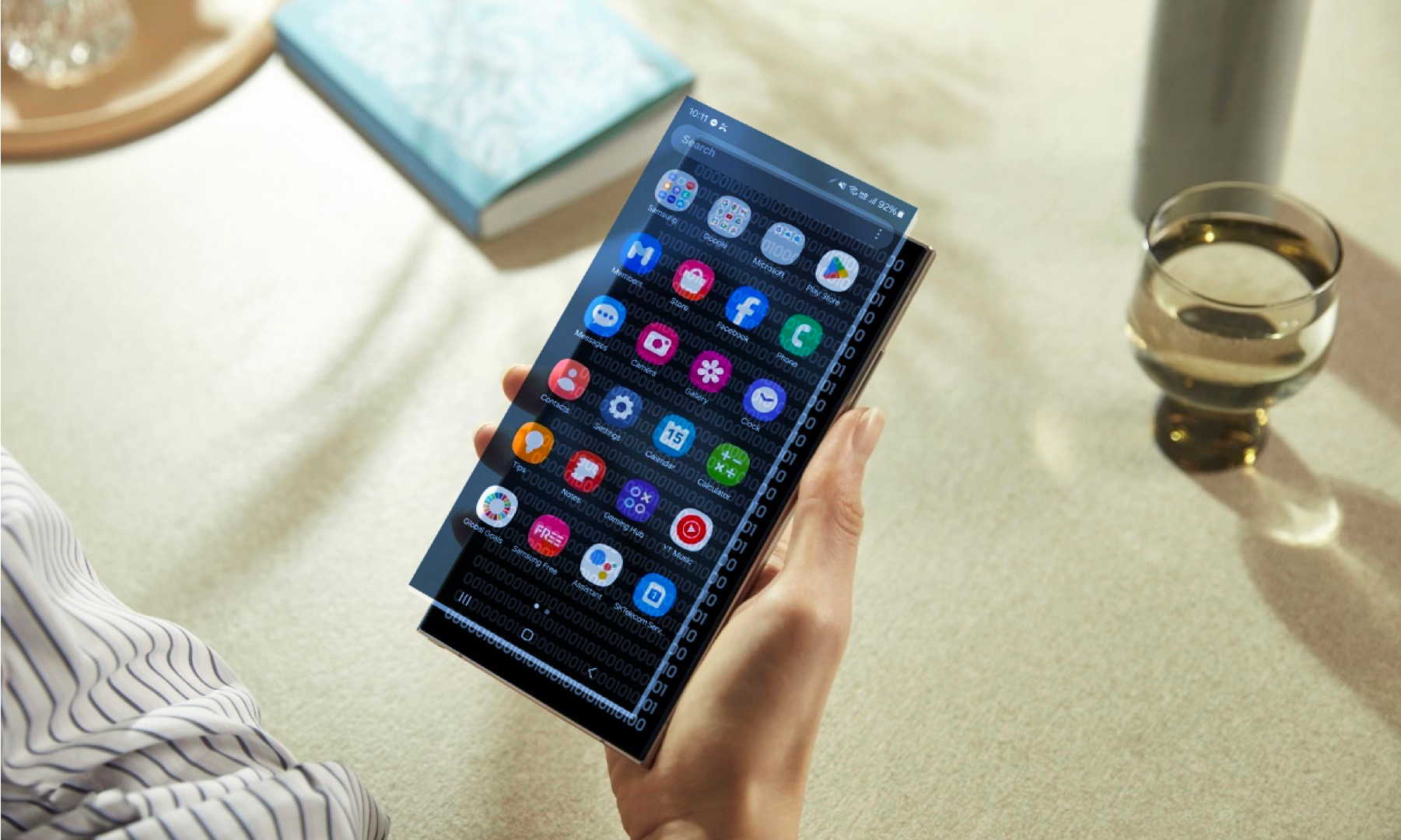Persona sosteniendo un dispositivo Samsung con código binario por debajo de una pantalla de aplicación superpuesta
